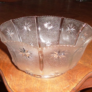 Op de afbeelding: Een glazen kom met een gegolfde rand en een stervormig patroon. De kom is mat en heeft een licht iriserende glans.