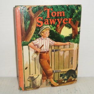 Puede incluir: Una portada de libro infantil vintage con un niño con un pincel, un cubo y un gato. El título del libro es "Tom Sawyer" en letras rojas y blancas.
