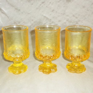May include: Three yellow glass goblets with a textured surface and a scalloped base.