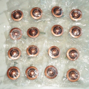 Puede incluir: Un juego de 18 pomos de armario de cobre con un diseño de círculos concéntricos. Los pomos están empaquetados individualmente en bolsas de plástico transparentes.