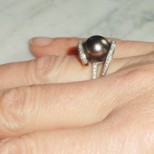 Pode incluir: Um anel de prata com uma grande p&eacute;rola preta e pequenos diamantes engastados na banda.