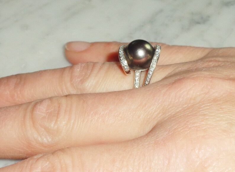 Pode incluir: Um anel de prata com uma grande p&eacute;rola preta e pequenos diamantes engastados na banda.