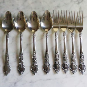 May include: Set of eight silver-plated spoons and forks with ornate floral designs. The spoons have a rounded bowl and the forks have four tines.