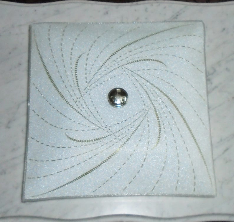 Pode incluir: Uma lumin&aacute;ria de teto quadrada branca com um padr&atilde;o de linhas em espiral e uma pe&ccedil;a central prateada.