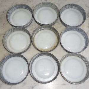 May include: Nine white enamel jar lids with silver metal rims. The lids are arranged in three rows of three.