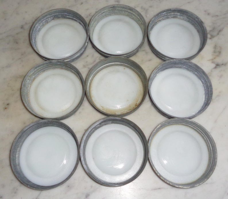May include: Nine white enamel jar lids with silver metal rims. The lids are arranged in three rows of three.