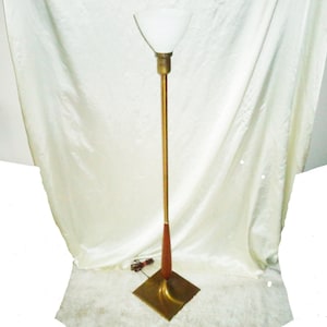 May include: A gold floor lamp with a white glass shade and a wooden base. The lamp is on a white rug.