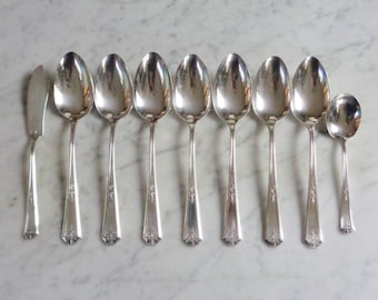 May include: A set of ten silver-plated spoons and a butter knife. The spoons have ornate handles with a floral design. The butter knife has a plain handle.