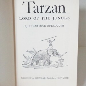 May include: A black and white illustration of Tarzan riding an elephant through the jungle. The book cover features the title "Tarzan, Lord of the Jungle" by Edgar Rice Burroughs and the publisher "Grosset & Dunlap, Publishers, New York".