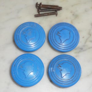 May include: Four blue ceramic cabinet knobs with a raised profile and a stylized profile of a person's head in the center. Each knob has three concentric circles around the profile.
