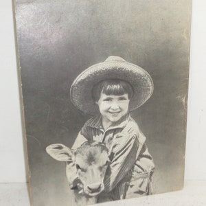 Peut inclure: Une jeune fille portant un chapeau de paille et une chemise &agrave; rayures tient un veau. La fille sourit et le veau regarde la cam&eacute;ra.