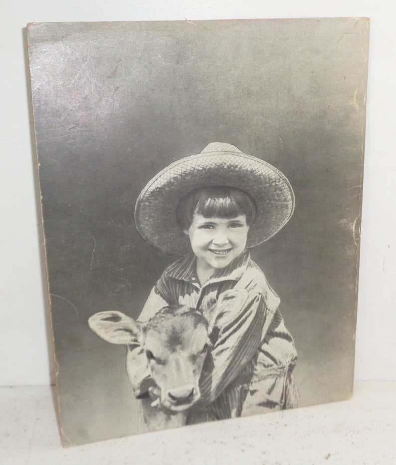 Peut inclure: Une jeune fille portant un chapeau de paille et une chemise &agrave; rayures tient un veau. La fille sourit et le veau regarde la cam&eacute;ra.