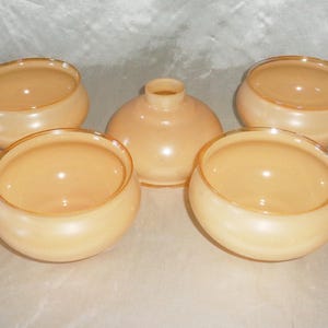 Puede incluir: Cinco pantallas de lámpara de vidrio en color melocotón pálido con un borde dorado. Las pantallas son redondas y tienen un acabado liso y brillante.