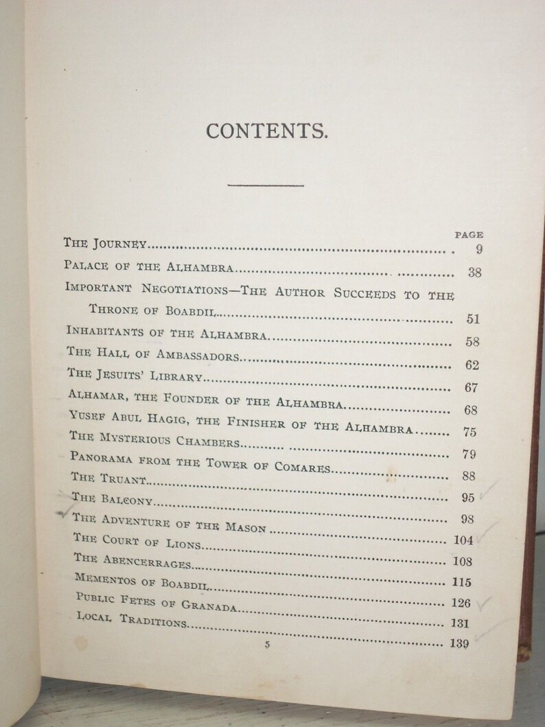 May include: A black and white book with the title "CONTENTS" printed in large, bold letters. The book lists the contents of the book, including the page numbers for each section. The sections include "The Journey", "Palace of the Alhambra", "Important Negotiations", "The Hall of Ambassadors", "The Jesuits' Library", "Alhamar, the Founder of the Alhambra", "Yusef Abul Hagig, the Finisher of the Alhambra", "The Mysterious Chambers", "Panorama from the Tower of Comares", "The Truant", "The Balcony", "The Adventure of the Mason", "The Court of Lions", "The Abencerrages", "Mementos of Boabdil", "Public Fetes of Granada", and "Local Traditions".