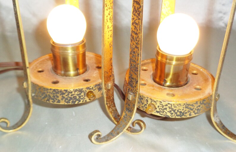 May include: A pair of antique gold-toned metal table lamps with clear glass bulbs. The lamps have a decorative, ornate design with a textured finish.