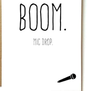 May include: A white greeting card with the words "BOOM. MIC DROP." in black lettering, and a small microphone illustration. The card is set against a brown envelope, with star-shaped confetti scattered around.