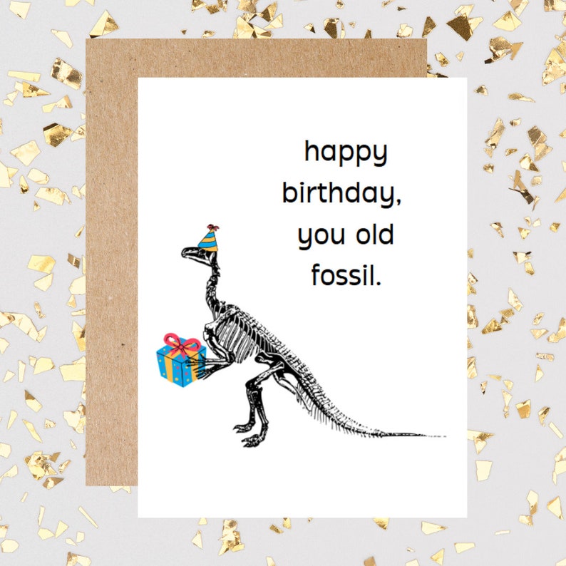 May include: A birthday card with a skeleton dinosaur wearing a party hat and holding a gift. The card reads "happy birthday, you old fossil."