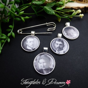 May include: A collection of silver-toned pendants with black and white portraits, along with a large safety pin. The pendants feature vintage photographs of people. The background is black, with green foliage and the text "Fairytales & Dreamz".