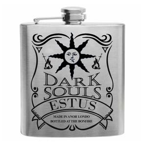 May include: A stainless steel flask with a black graphic design featuring a sun with a face, swords, and the words "DARK SOULS ESTUS". The text "MADE IN ANOR LONDO BOTTLED AT THE BONFIRE" is also included.