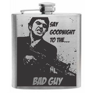 May include: Stainless steel flask with a black graphic of a man holding a gun, with the text "SAY GOODNIGHT TO THE... BAD GUY". The flask has a hinged top and a silver finish.