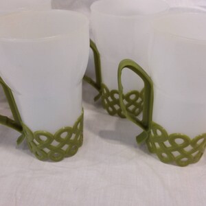 May include: Set of four white plastic cups with green handles and green decorative bands around the bottom.