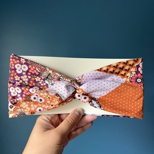 May include: A brown, purple, and white patterned headband with a twisted knot design.