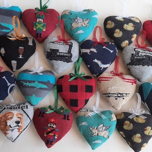 May include: A collection of heart-shaped ornaments with various patterns and designs. Some feature plaid, dogs, airplanes, and ducks. Each ornament has a ribbon loop for hanging, making them suitable for holiday or everyday decor.