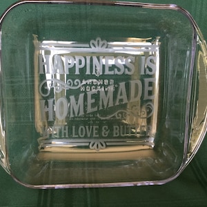 Könnte beinhalten: Klarer Glas-Backform mit geätztem Text: „HAPPINESS IS HOMEMADE WITH LOVE & BUTTER“. Die Form hat eine rechteckige Form mit abgerundeten Ecken und Griffen. Der Text ist in einer dekorativen Schriftart.