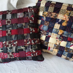 May include: Two decorative pillows made from woven neckties. One pillow is red, black, and white. The other pillow is blue, brown, and white.