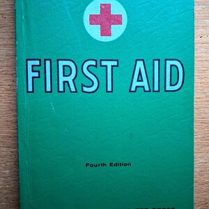 May include: A green book titled FIRST AID with a red cross symbol. The cover text reads Fourth Edition and THE AMERICAN NATIONAL RED CROSS. The book has a textured green cover and is a manual for emergency medical procedures and safety.