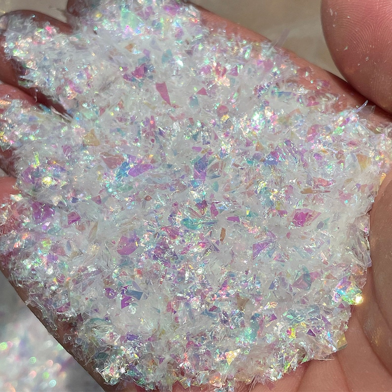 Op de afbeelding: Een close-up van iriserende witte glittervlokken, perfect om glans toe te voegen aan knutselprojecten en harsprojecten.