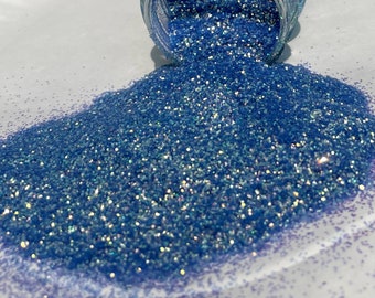Op de afbeelding: Een hoop lichtblauwe, iriserende glitter, met een vleugje paars, die uit een doorzichtige pot stroomt.