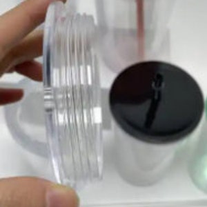 Pu&ograve; includere: Primo piano di un coperchio in plastica trasparente con un coperchio nero in cima. Il coperchio ha una superficie testurizzata ed &egrave; progettato per un bicchiere.