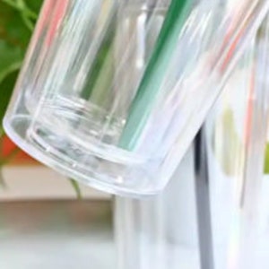 Pu&ograve; includere: Primo piano di un bicchiere di plastica trasparente con un design a doppia parete. Il bicchiere &egrave; vuoto e ha una finitura liscia e lucida.