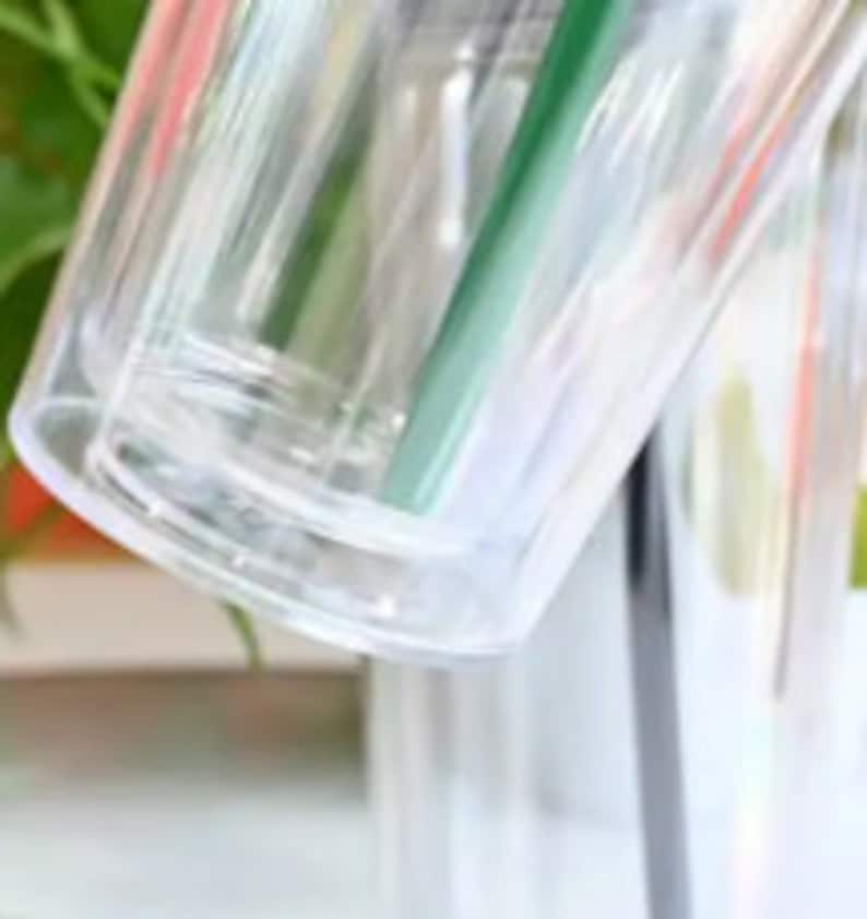 Pu&ograve; includere: Primo piano di un bicchiere di plastica trasparente con un design a doppia parete. Il bicchiere &egrave; vuoto e ha una finitura liscia e lucida.