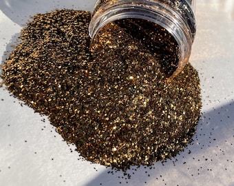 May include: A close-up of a jar of gold glitter being poured out onto a white surface. The glitter is a fine, shimmery gold color.