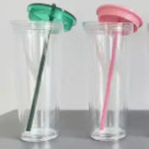 Pu&ograve; includere: Due bicchieri di plastica trasparente con coperchi e cannucce. Il bicchiere a sinistra ha un coperchio verde e una cannuccia nera. Il bicchiere a destra ha un coperchio rosa e una cannuccia rosa.