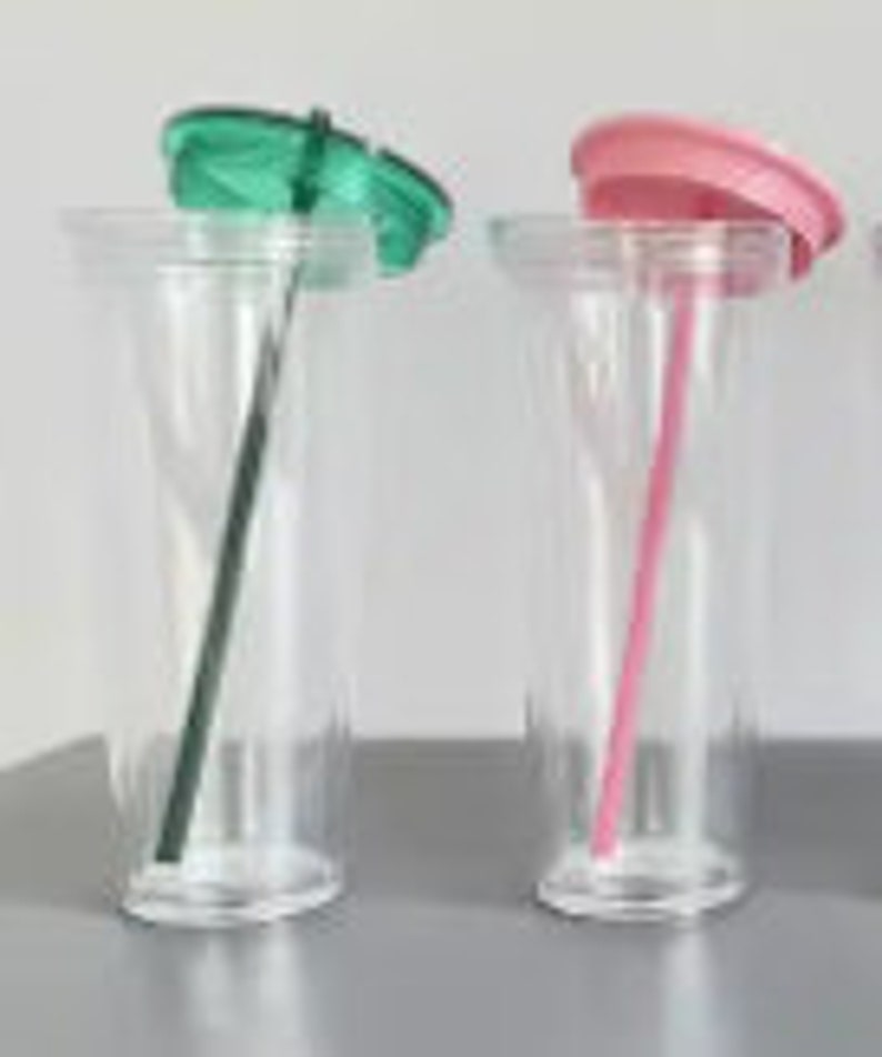 Pu&ograve; includere: Due bicchieri di plastica trasparente con coperchi e cannucce. Il bicchiere a sinistra ha un coperchio verde e una cannuccia nera. Il bicchiere a destra ha un coperchio rosa e una cannuccia rosa.