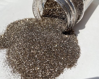 Op de afbeelding: Een close-up van een pot met losse glitter, met een metallic bronzen kleur. De glitter stroomt uit de pot op een wit oppervlak.