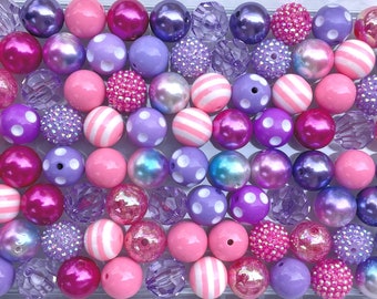 May include: A collection of various beads in shades of pink, purple, and lavender. The beads include solid colors, polka dots, stripes, and textured surfaces. Some beads have a shiny, iridescent finish, while others are matte.