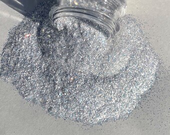 May include: A pile of iridescent silver glitter, with a clear plastic jar spilling glitter onto the white surface.