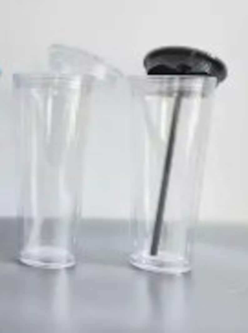 Pu&ograve; includere: Due bicchieri di plastica trasparente con coperchi. Un bicchiere ha un coperchio nero e una cannuccia nera. L'altro bicchiere ha un coperchio trasparente.