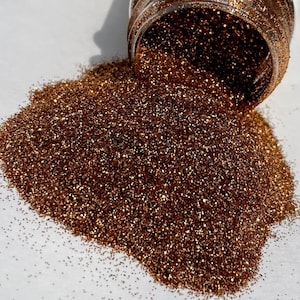 May include: A pile of fine copper glitter, with a small amount spilling from a clear jar.