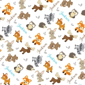 May include: A white baby blanket with a repeating pattern of woodland animals, including foxes, owls, raccoons, deer, bears, and moose. The blanket is personalized with the name "Jackson" repeated throughout the design. The blanket measures 30 inches by 40 inches.