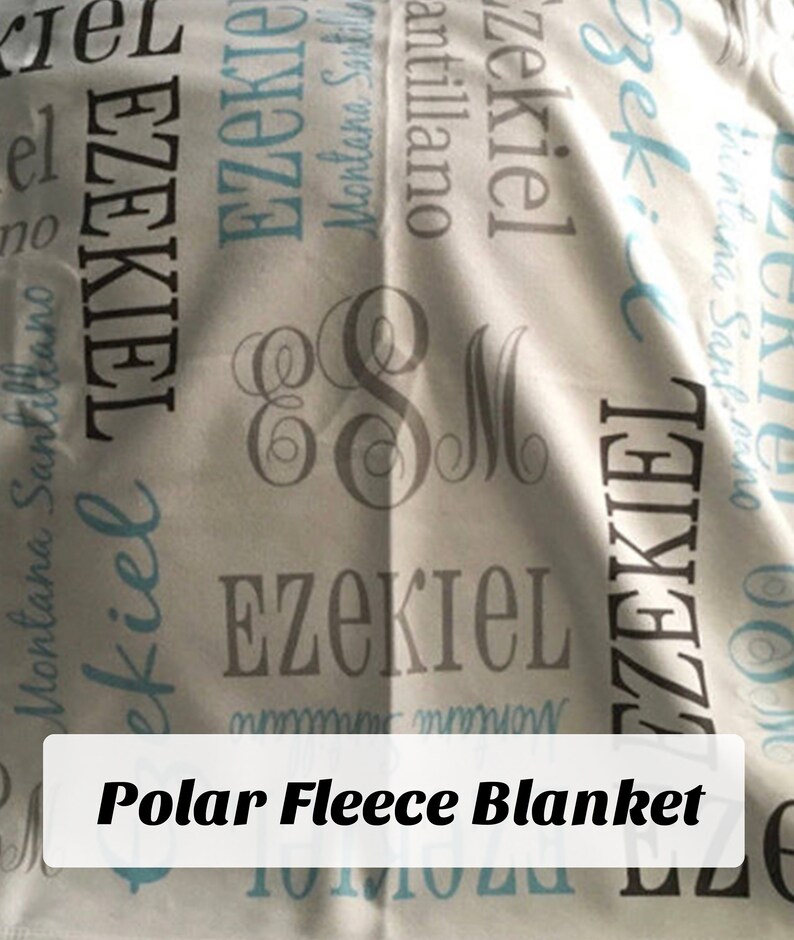 Op de afbeelding: Een wit fleece deken met de naam "Ezekiel" bedrukt in grijze en blauwe letters. Het deken heeft ook een monogram met de letters "E" en "M" in grijs.