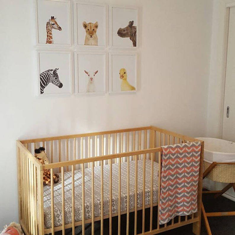 Puede incluir: Una cuna de madera con una s&aacute;bana estampada en blanco y gris y una manta de chevron coral y gris. Hay estampados de animales enmarcados en la pared sobre la cuna.