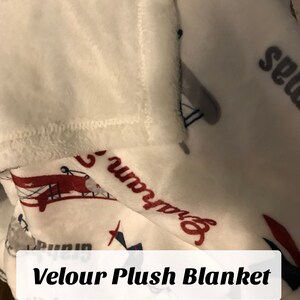 Op de afbeelding: Witte velours pluche deken met een rood, wit en blauw vliegtuigontwerp. De deken heeft de tekst "Runway" en "Seagull" erop gedrukt.