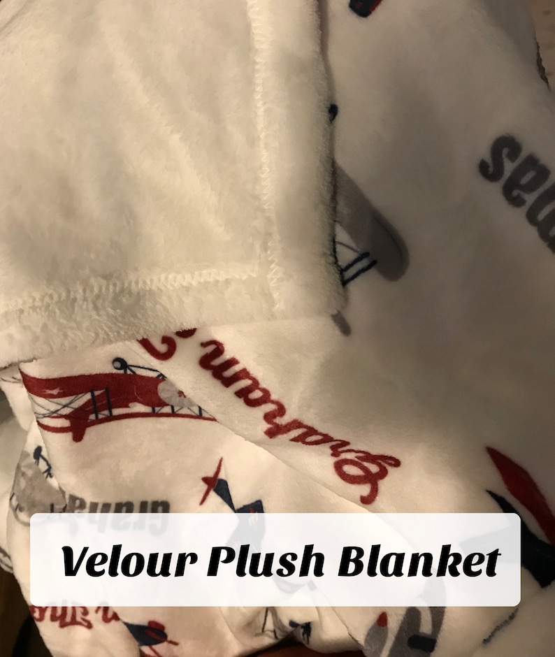 Op de afbeelding: Witte velours pluche deken met een rood, wit en blauw vliegtuigontwerp. De deken heeft de tekst "Runway" en "Seagull" erop gedrukt.