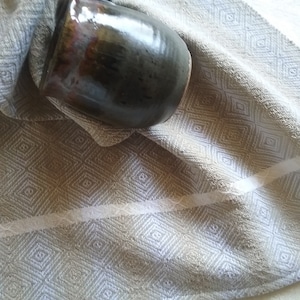 May include: A beige kitchen towel with a white diamond pattern. The towel is folded and a brown ceramic jug is resting on top of it.