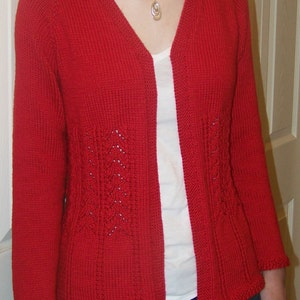 May include: A red knitted cardigan with a v-neck and a delicate lace pattern on the front. The cardigan is worn over a white t-shirt and blue jeans.
